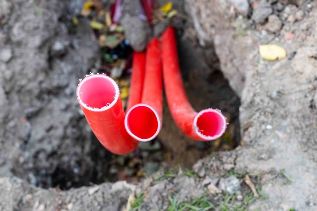 red plastic conduit pipes for outdoor underground electrical wiring in trench closeup