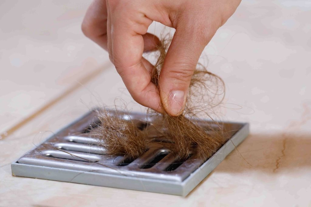 Woman removing hair clump from the shower drain.