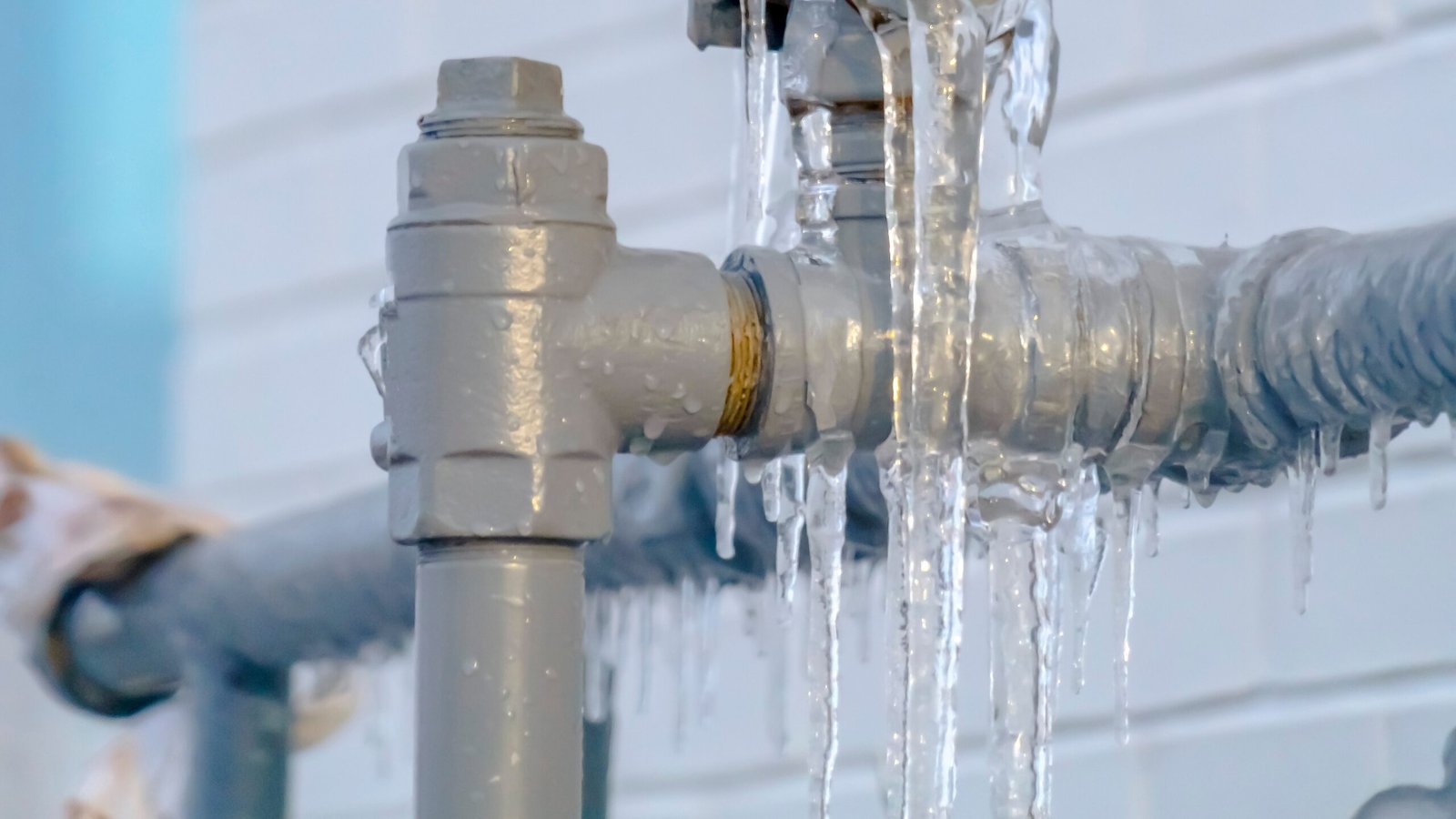 frozen pipes - Close up of a gray metal pipe covered with ice against a white brick wall